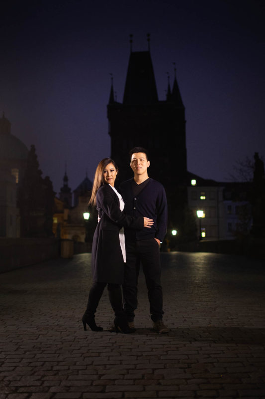 Prague Charles Bridge at night, blue sky, stylish young couple wearing black, gas lamps