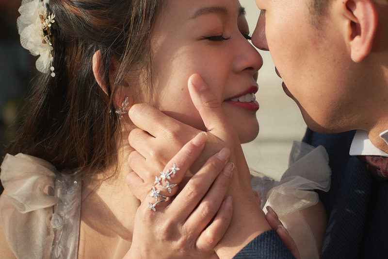 A stylishly dressed couple share an intimate embrace where only their lips and the couples hands lovingly caressing one-another are seen.