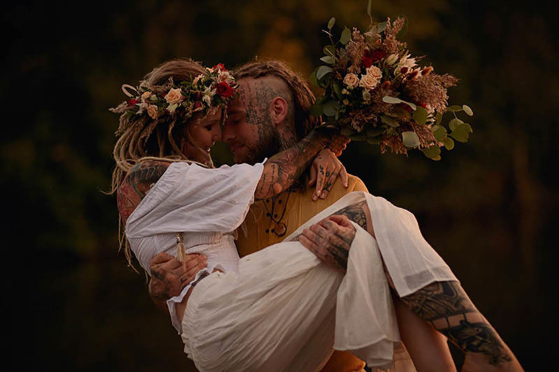 A tattooed and dreadlock couple share a long embrace as the woman - holding a bouquet - is held aloft.