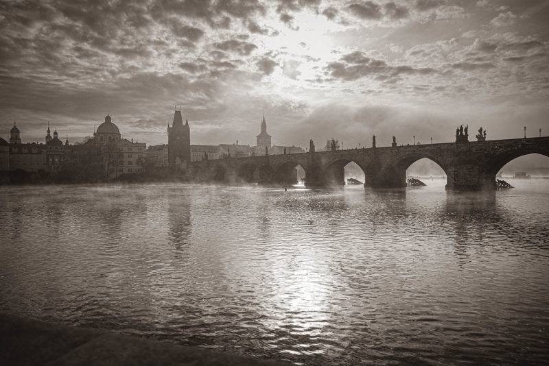 Monochrome image of the Charles Bridge as the mist rises above the Vltava below following the sunrise over Prague.